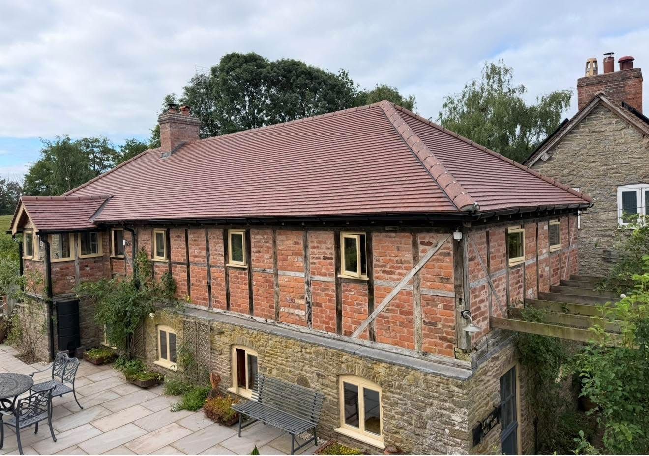 Timber-framed brick range finished with a new hipped clay tiled roof above an older stone ground floor