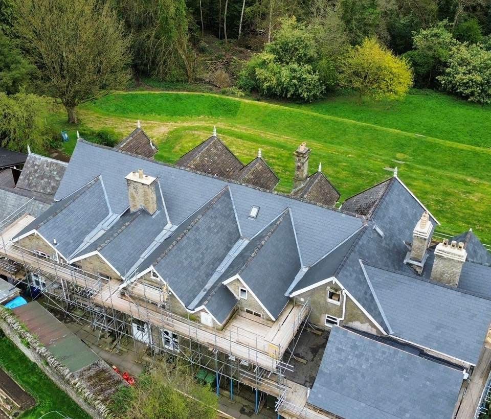 Aerial view of a completed natural slate re-roof on a large multi-gabled period building, with lead valleys, stone chimneys and finials retained